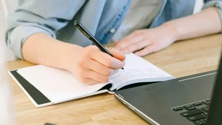 Como fazer um resumo: Dicas essenciais para saber como escrever um resumo 1 Como Fazer um Resumo: pessoa escrevendo em um caderno ao lado de um laptop.